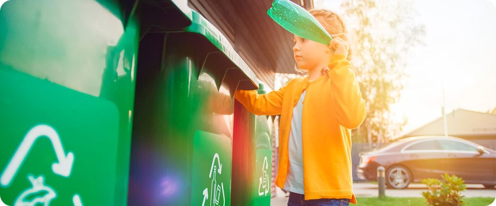 Criança jogando garrafa de plástico verde no lixo reciclável.